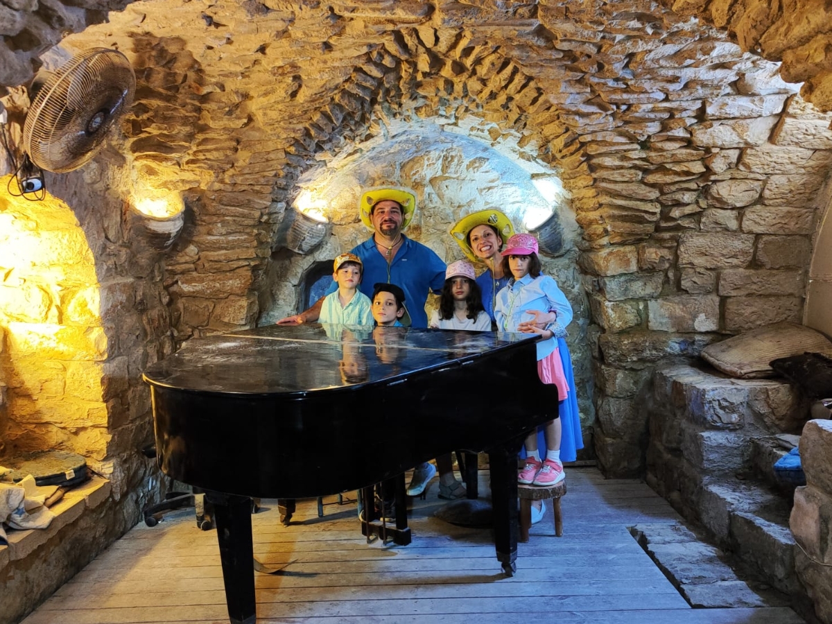 משפחה עם כובעים צהובים ליד פסנתר במרתף אבן בצפת